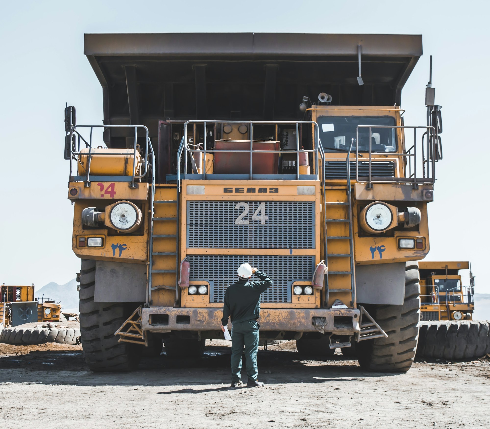 A worker in workwear standing in front of a giant quarry haul truck.