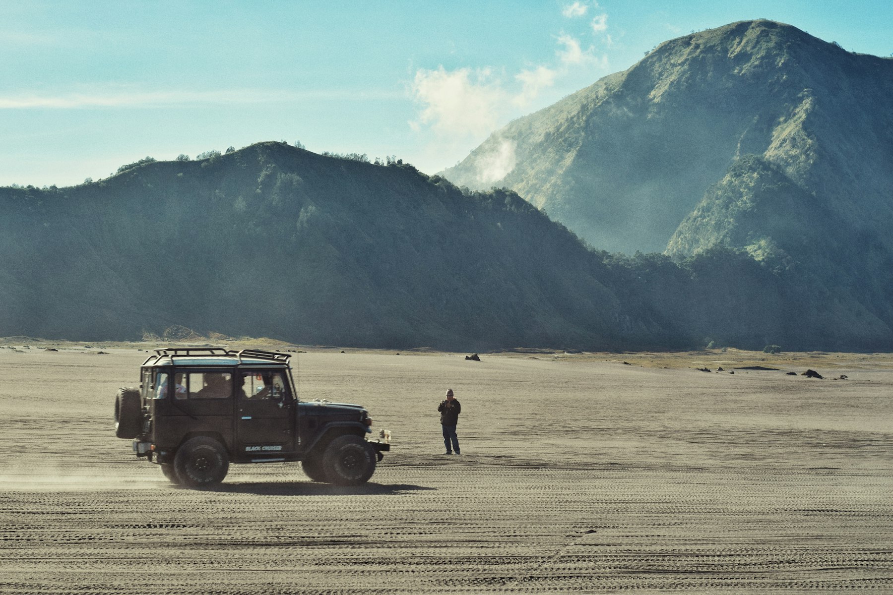 A classic 40 Series Land Cruiser on a dry lake bed, mountains behind.