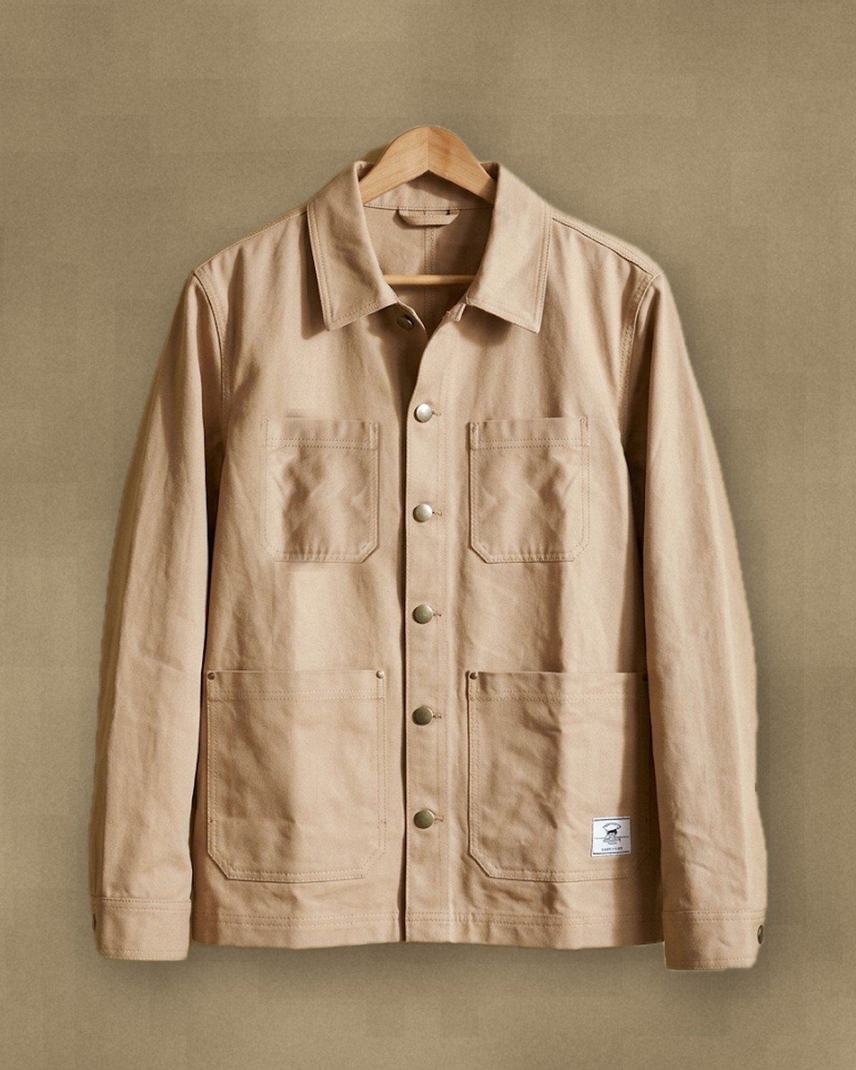 The sand Chore Jacket on a hanger, woven label on the hem.